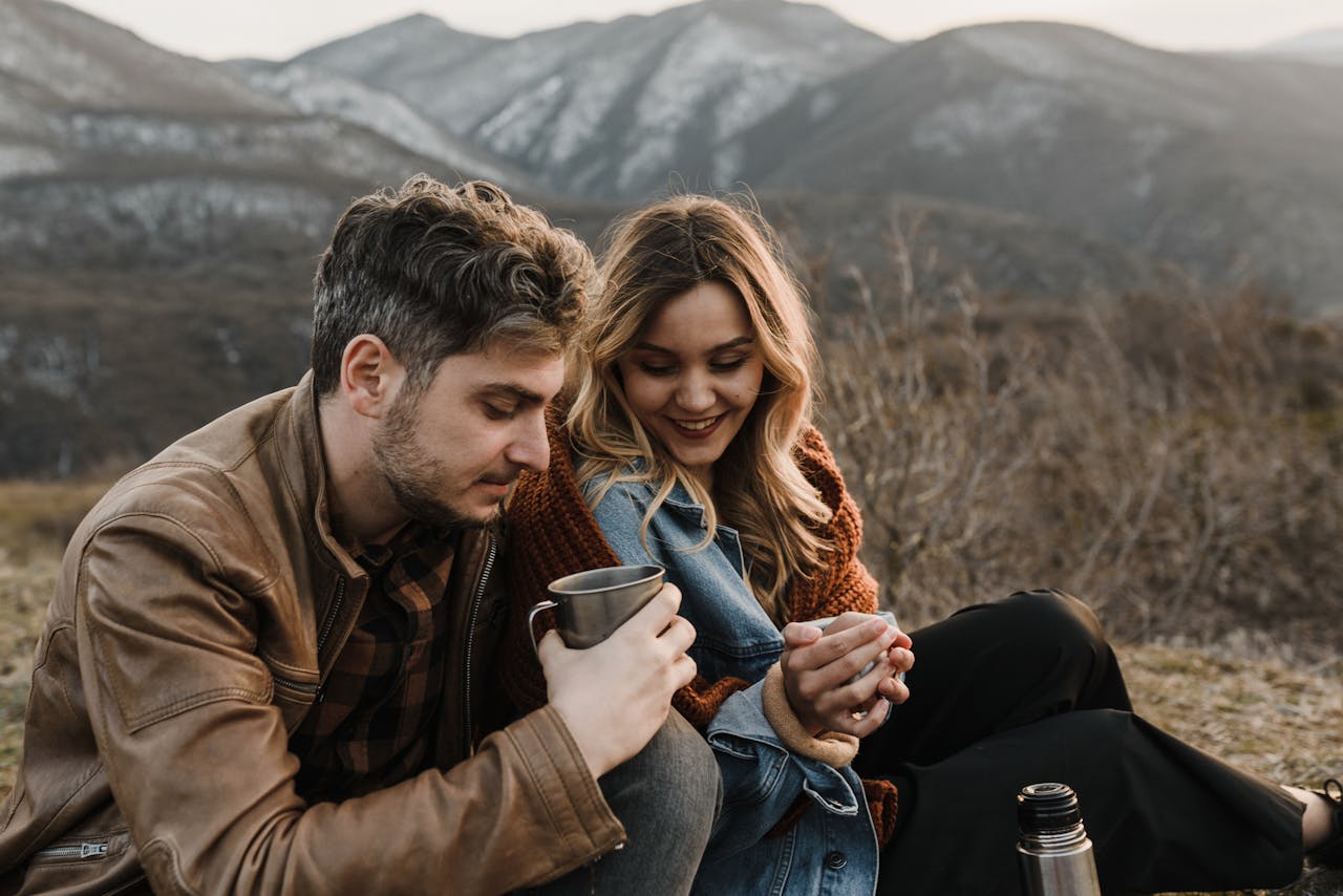 A couple enjoying a cozy moment with coffee outdoors in a scenic mountain setting.